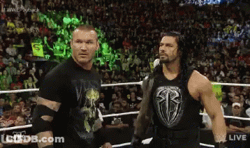 Two Wrestlers Are Standing Next To Each Other In A Wrestling Ring With A Crowd In The Background . GIF
