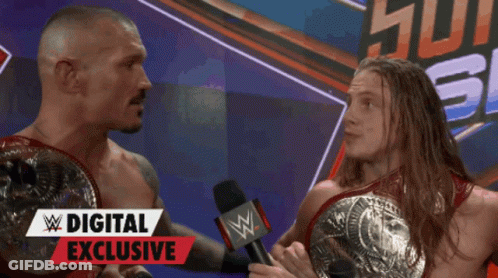 Two Wrestlers Are Talking In Front Of A Digital Exclusive Banner GIF