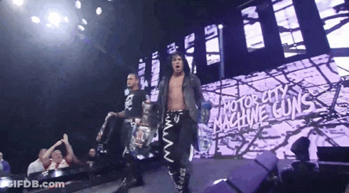 Two Wrestlers Are Walking Down A Stage With A Sign That Says Motor City Machine Guns GIF