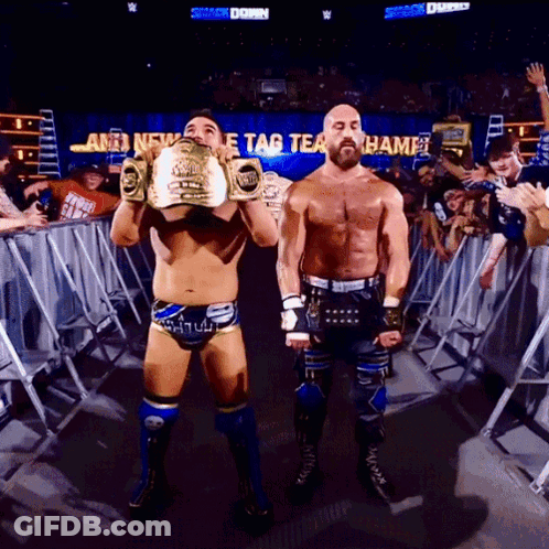 Two Wrestlers By Sign Saying Tag Team Champ GIF