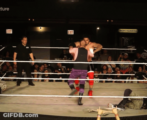 Two Wrestlers In A Ring With An Exit Sign Behind Them GIF