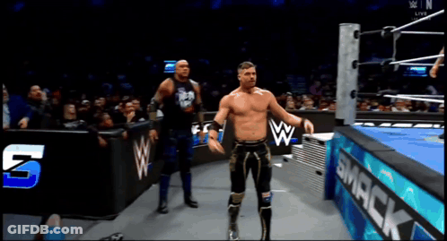 Two Wrestlers In A Wrestling Ring With A Smack Sign In The Background GIF