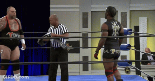 Two Wrestlers In Ring With Referee Holding Remote GIF