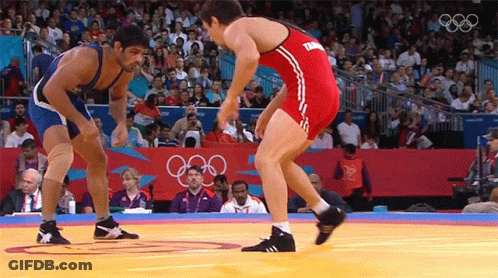 Two Wrestlers Wrestling In Front Of Crowd With Olympic Rings GIF