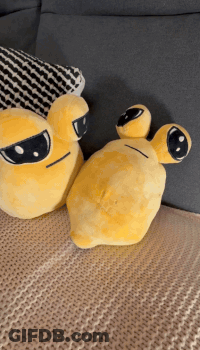 Two Yellow Stuffed Animals Are Sitting On A Bed Next To A Pillow GIF