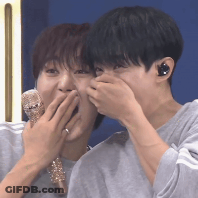 Two Young Men Are Covering Their Mouths With Their Hands While Holding A Microphone . GIF