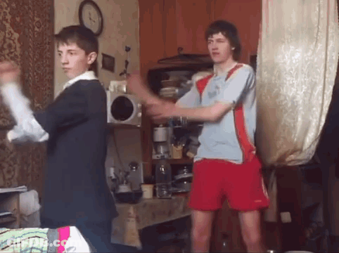 Two Young Men Are Dancing In A Living Room With A Clock In The Background . GIF
