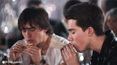 Two Young Men Are Eating Hamburgers In A Restaurant . GIF