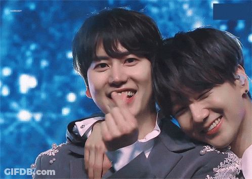 Two Young Men Are Hugging Each Other And One Of Them Is Making A Heart Shape With His Finger GIF