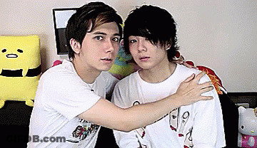 Two Young Men Are Hugging Each Other In Front Of A Hello Kitty Doll . GIF