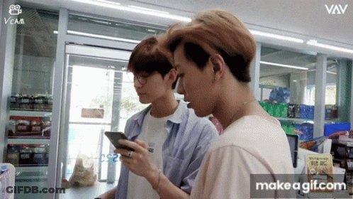 Two Young Men Are Looking At Their Cell Phones In A Store With The Words Make A Gif.com On The Bottom Right GIF