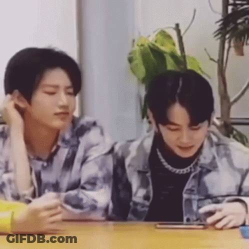 Two Young Men Are Sitting At A Table With A Cell Phone . GIF