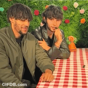 Two Young Men Are Sitting At A Table With A Checkered Tablecloth . GIF