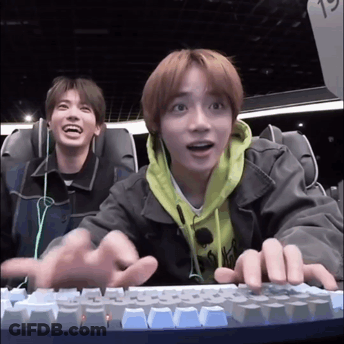 Two Young Men Are Sitting In A Roller Coaster And Playing A Video Game On A Keyboard . GIF