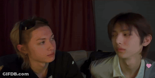 Two Young Men Are Sitting Next To Each Other And Looking At Each Other In A Dark Room . GIF