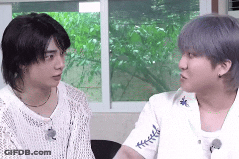 Two Young Men Are Sitting Next To Each Other And Looking At Each Other In Front Of A Window . GIF