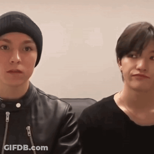 Two Young Men Are Sitting Next To Each Other And Looking At The Camera . One Of The Men Is Wearing A Beanie . GIF