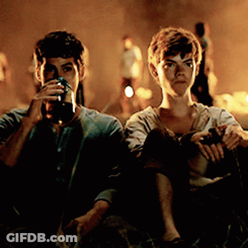 Two Young Men Are Sitting Next To Each Other Drinking From Glasses GIF