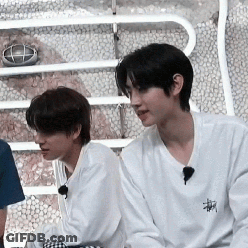 Two Young Men Are Sitting Next To Each Other In A Room . GIF