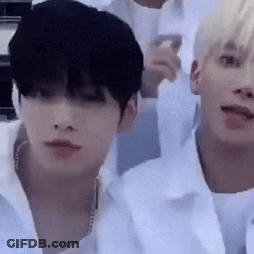 Two Young Men Are Sitting Next To Each Other In A Room And One Of Them Is Wearing A White Shirt . GIF