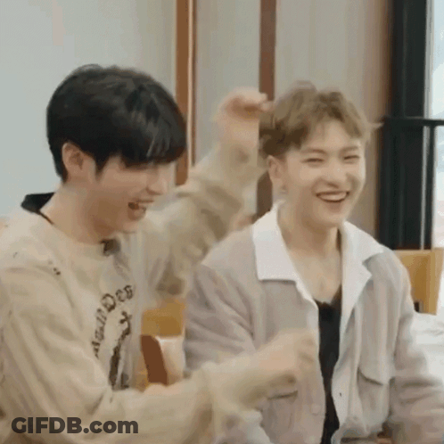 Two Young Men Are Sitting Next To Each Other In A Room Laughing And Playing With Each Other . GIF