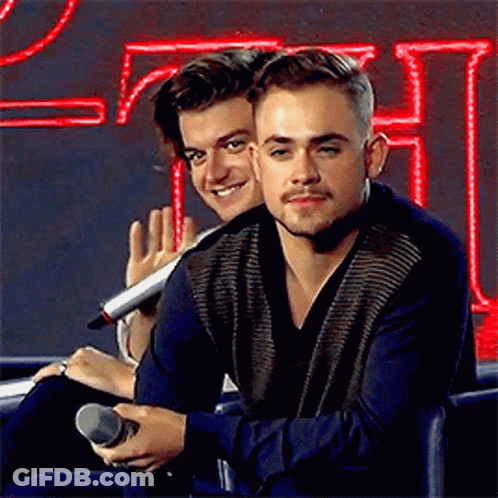Two Young Men Are Sitting Next To Each Other In Front Of A Microphone . GIF