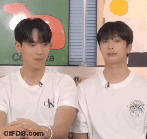 Two Young Men Are Sitting Next To Each Other In Front Of A Wall . GIF