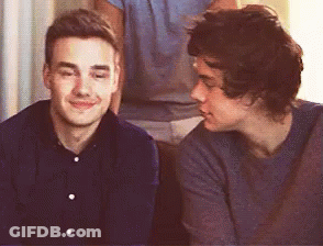 Two Young Men Are Sitting Next To Each Other On A Couch And Looking At Each Other . GIF