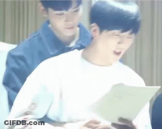 Two Young Men Are Sitting Next To Each Other On A Couch And One Of Them Is Reading A Book . GIF