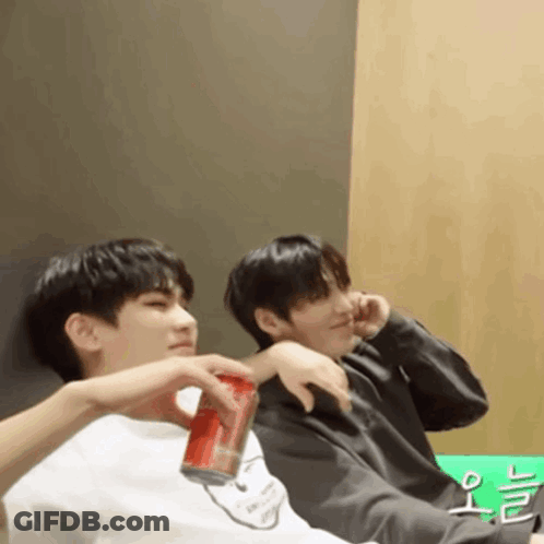 Two Young Men Are Sitting Next To Each Other One Is Holding A Can Of Soda GIF