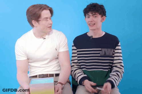 Two Young Men Are Sitting Next To Each Other With One Wearing A Sweater With Jw On It GIF