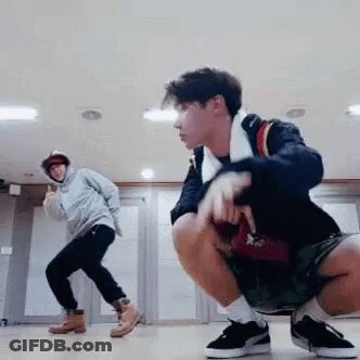 Two Young Men Are Squatting On The Floor In A Room While One Of Them Is Dancing . GIF