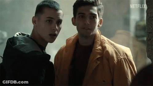 Two Young Men Are Standing Next To Each Other In A Dark Room . One Of The Men Is Wearing A Yellow Jacket . GIF