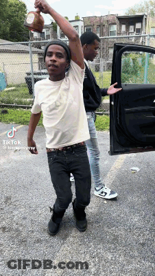 Two Young Men Are Standing Next To Each Other In Front Of A Car And One Is Holding A Bottle In His Hand . GIF