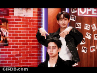 Two Young Men Are Standing Next To Each Other In Front Of A Red Brick Wall . GIF