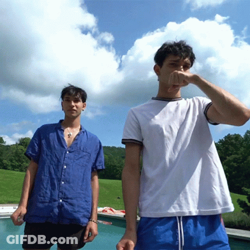 Two Young Men Are Standing Next To Each Other Near A Pool GIF