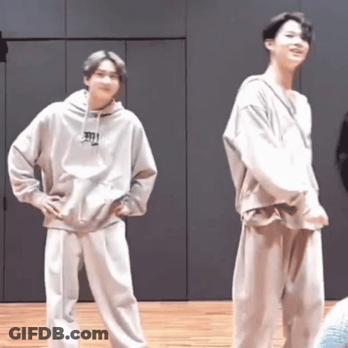 Two Young Men Are Standing Next To Each Other On A Wooden Floor In A Room . GIF