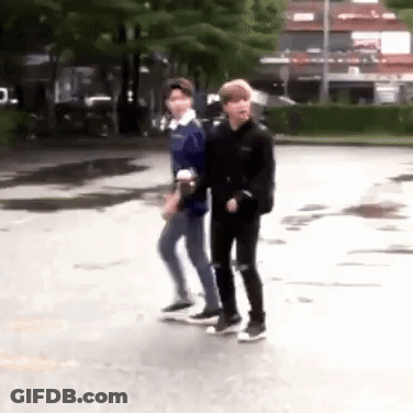 Two Young Men Are Walking Down A Street . GIF