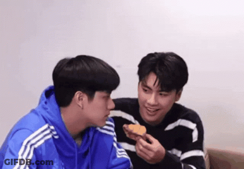 Two Young Men Eating Croissant On Couch GIF