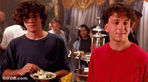 Two Young Men Holding Plates Of Food And Smiling GIF