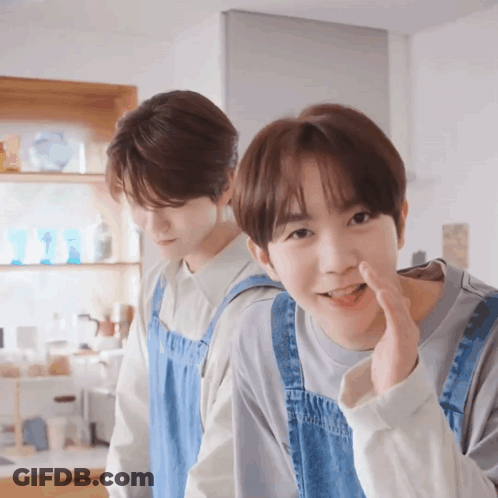 Two Young Men In Aprons Standing Together GIF