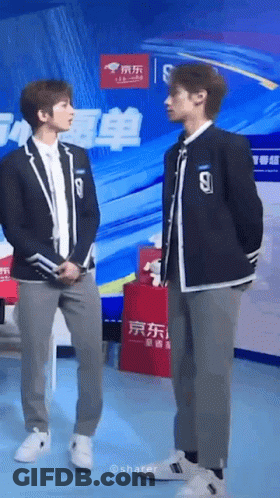 Two Young Men In Suits Are Standing Next To Each Other In Front Of A Large Screen . GIF