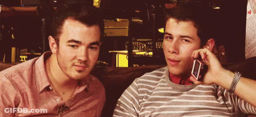 Two Young Men On Couch One On Phone GIF