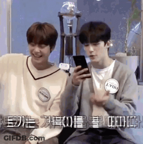 Two Young Men Sitting Next To Each Other One Looking At Phone GIF