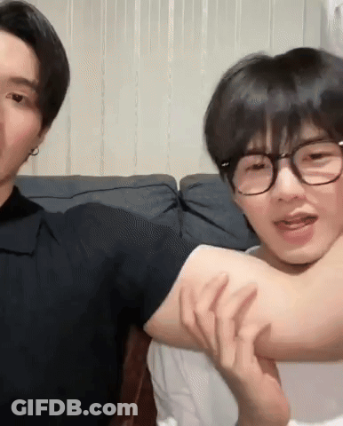 Two Young Men Sitting On Couch One Holding Other's Arm GIF