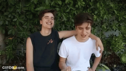 Two Young Men Sitting With Arms Around Each Other Smiling GIF