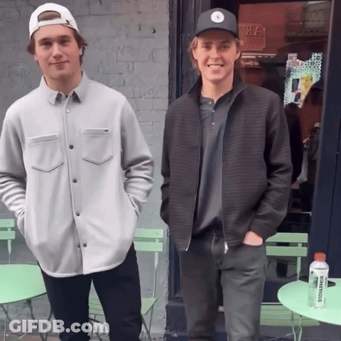 Two Young Men Standing In Front Of A Store With A Bottle Of Juice That Says ' Tropicana ' On It GIF
