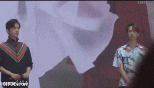 Two Young Men Standing Next To Each Other On Stage In Front Of Large Screen GIF