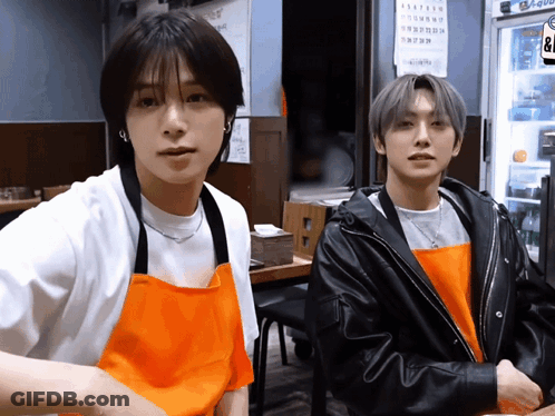 Two Young Men Wearing Aprons Are Standing Next To Each Other In Front Of A Fridge That Says ' Coca Cola ' On It GIF
