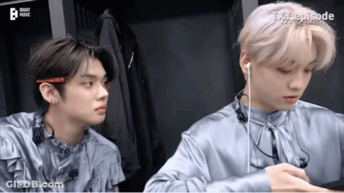 Two Young Men Wearing Earphones Sitting Next To Each Other GIF